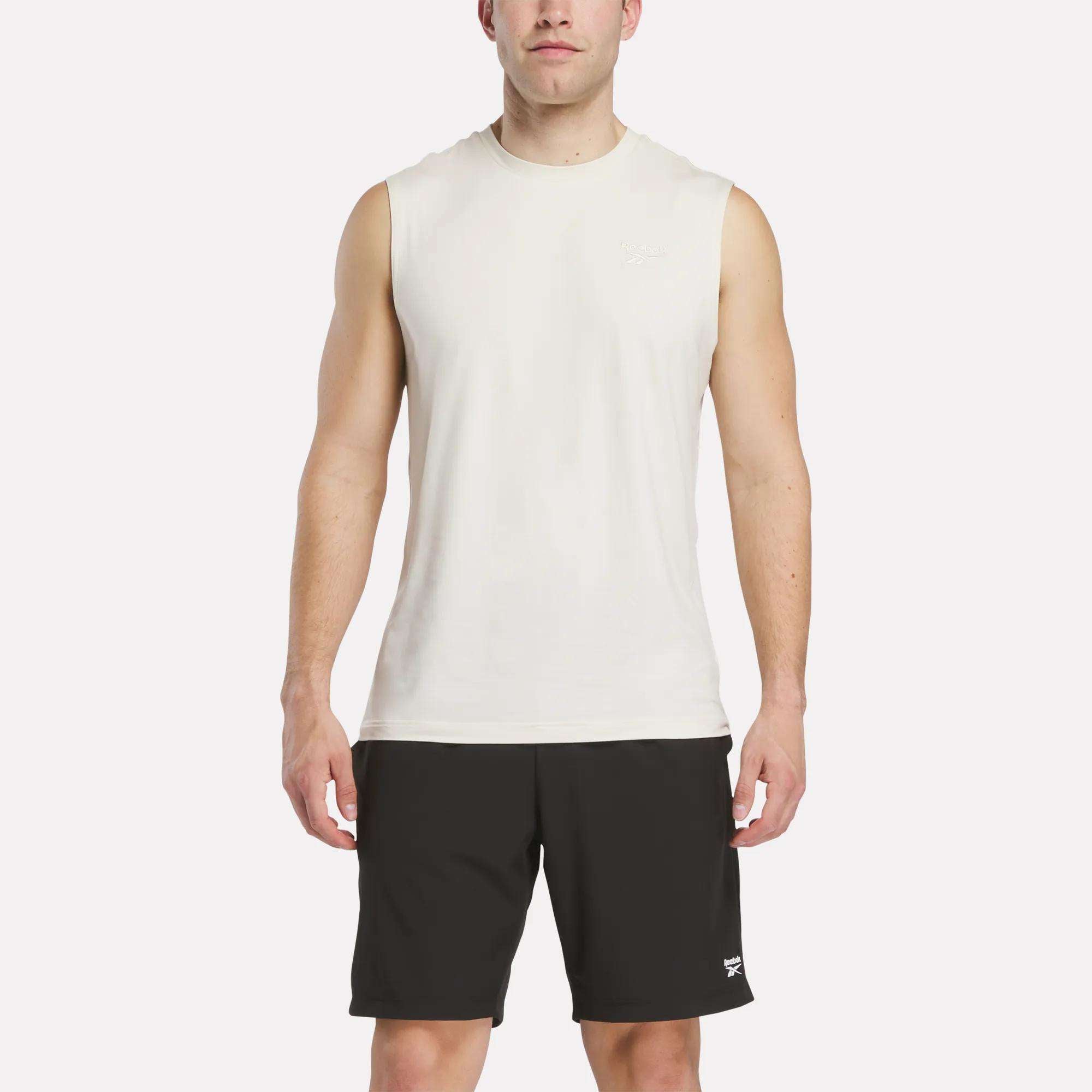 A man faces forward wearing a Reebok Men's Elite Sleeveless Top and black athletic shorts against a plain white background.