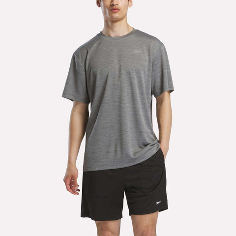 A person in a Reebok Men's Director Short Sleeve Top and black shorts with small Reebok logos stands against a plain light background.