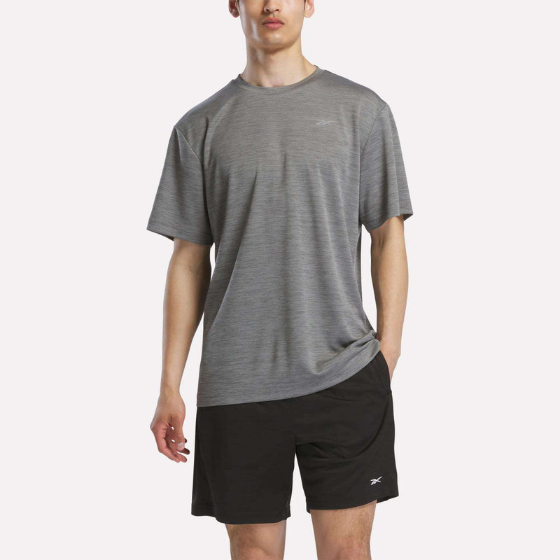 A person in a Reebok Men's Director Short Sleeve Top and black shorts with small Reebok logos stands against a plain light background.