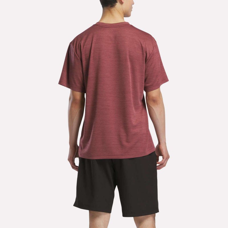 A person faces away, wearing a maroon Reebok Men's Director Short Sleeve Top and black shorts against a plain white background.