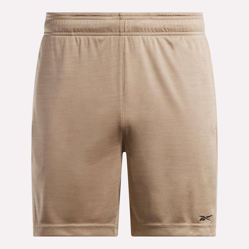 The Reebok Men's Inclination Shorts feature tan, soft fabric and an elastic waistband. A small black Reebok logo accents the lower left leg. These athletic shorts are shown against a plain, light background.