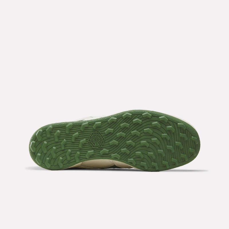 A Reebok x Manors Club C Revenge Golf Shoe, inspired by Manors golf footwear, is shown from the bottom, revealing its green textured sole with a subtle starburst detail near the center. The rest of the shoe is only faintly visible against a light background.