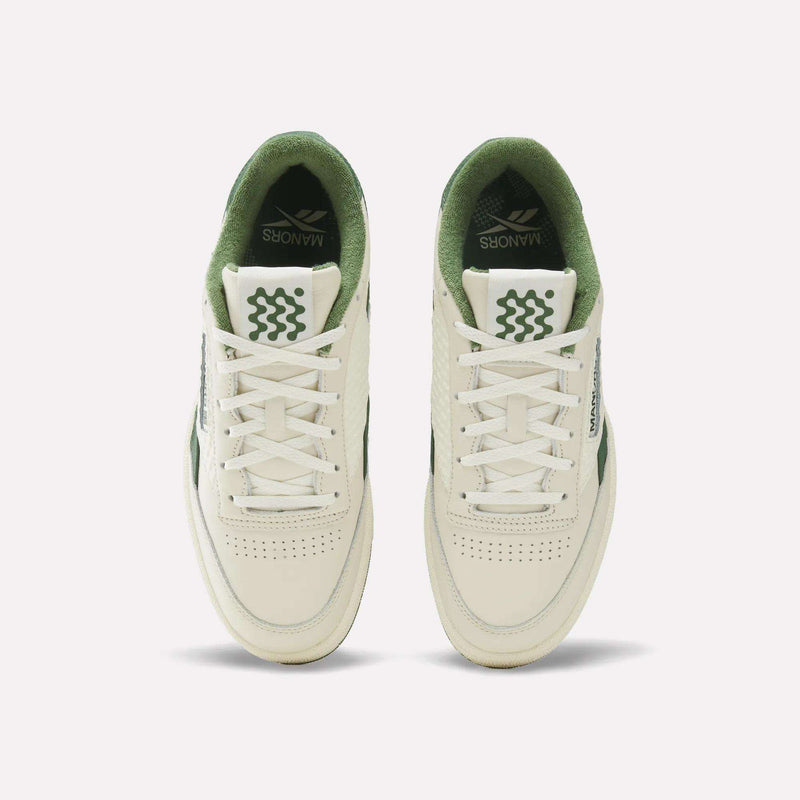 Top view of a pair of Reebok x Manors Club C Revenge Golf Shoes in cream and green with white laces. The tongue and inner lining are green, featuring wavy green lines and the word “MANNORS,” reminiscent of the premium collaboration between Reebok and Manors golf shoes. The shoes have perforated toe boxes.
