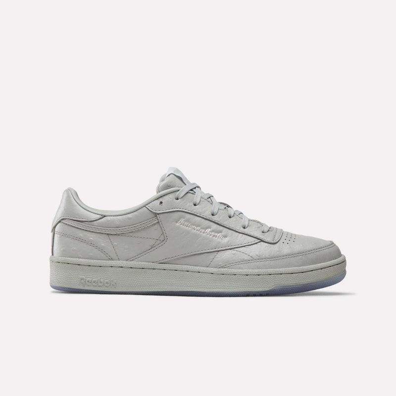 A Grey/Grey Reebok x BBC Club C 85 shoe featuring a low-top silhouette, flat sole, and lace-up closure—crafted from premium materials to celebrate Reebok’s heritage—is displayed in a side profile against a plain white background.