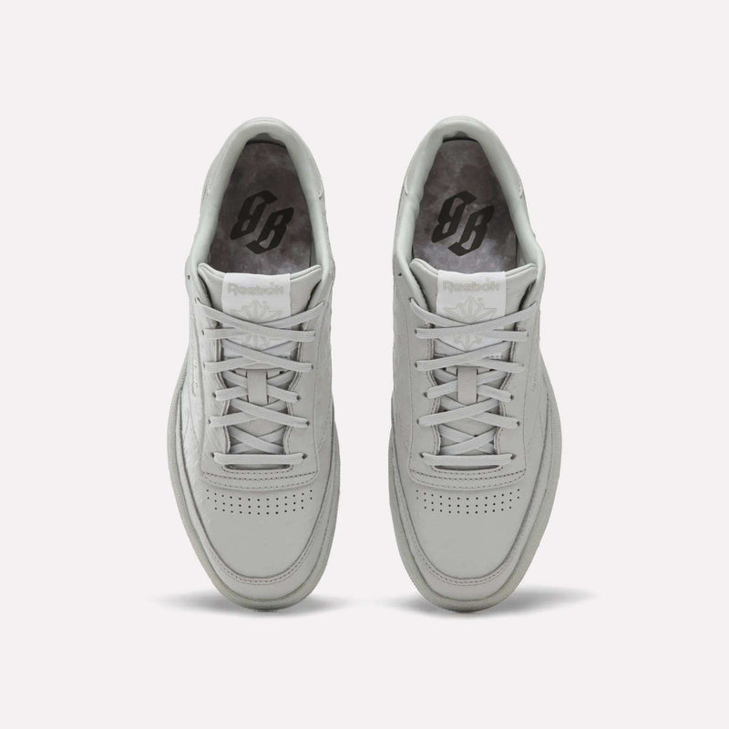 A pair of Reebok x BBC Club C 85 Shoes in white are displayed side by side on a light background, viewed from above to showcase their laces, perforated toe boxes, and grey insoles featuring a black printed Reebok logo. Expertly crafted from premium materials, these heritage sneakers highlight the collaboration between Reebok and BBC.