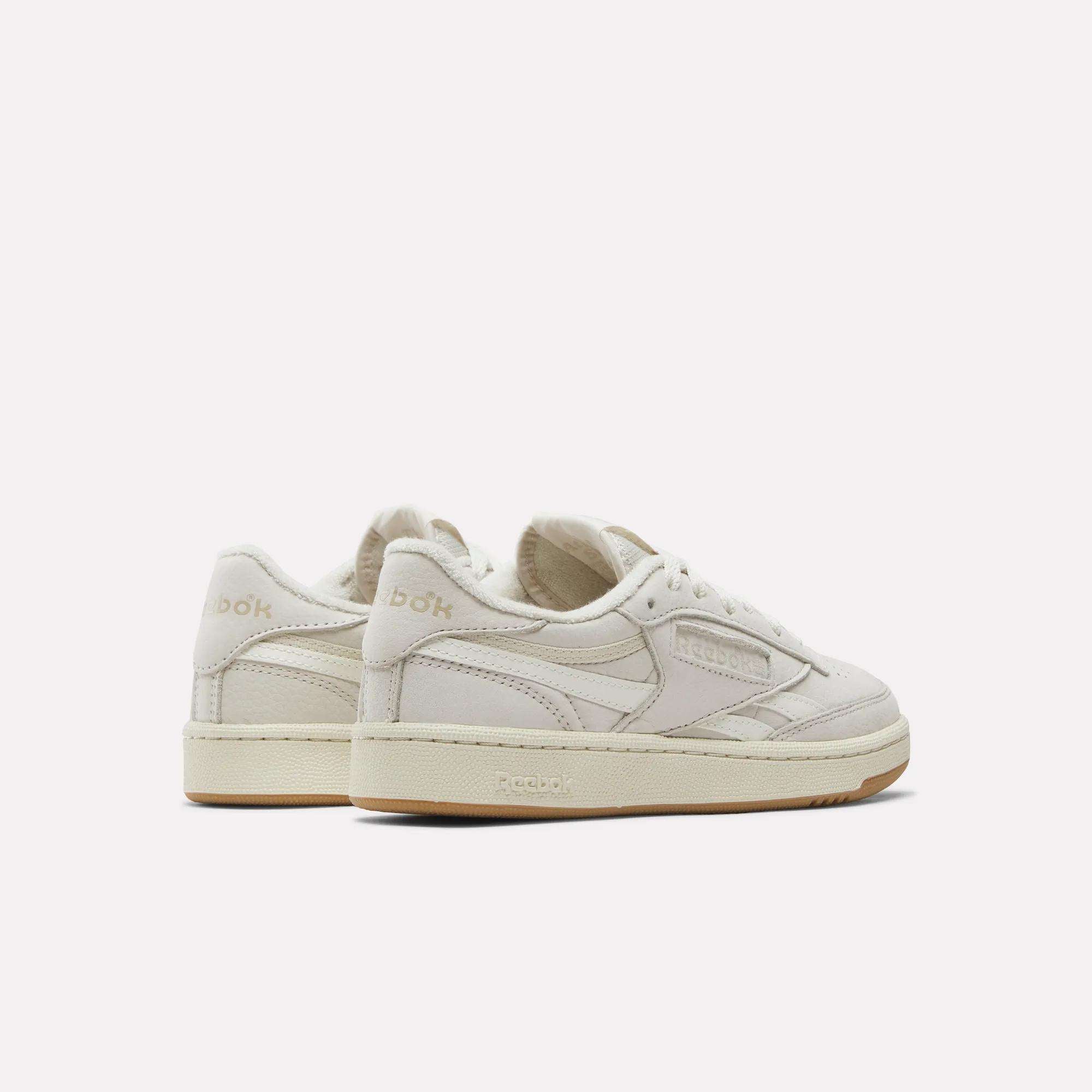 A pair of Reebok Women's Club C Revenge Shoes featuring off-white uppers, beige soles, and nubuck leather accents is shown from the back and side against a plain white background.