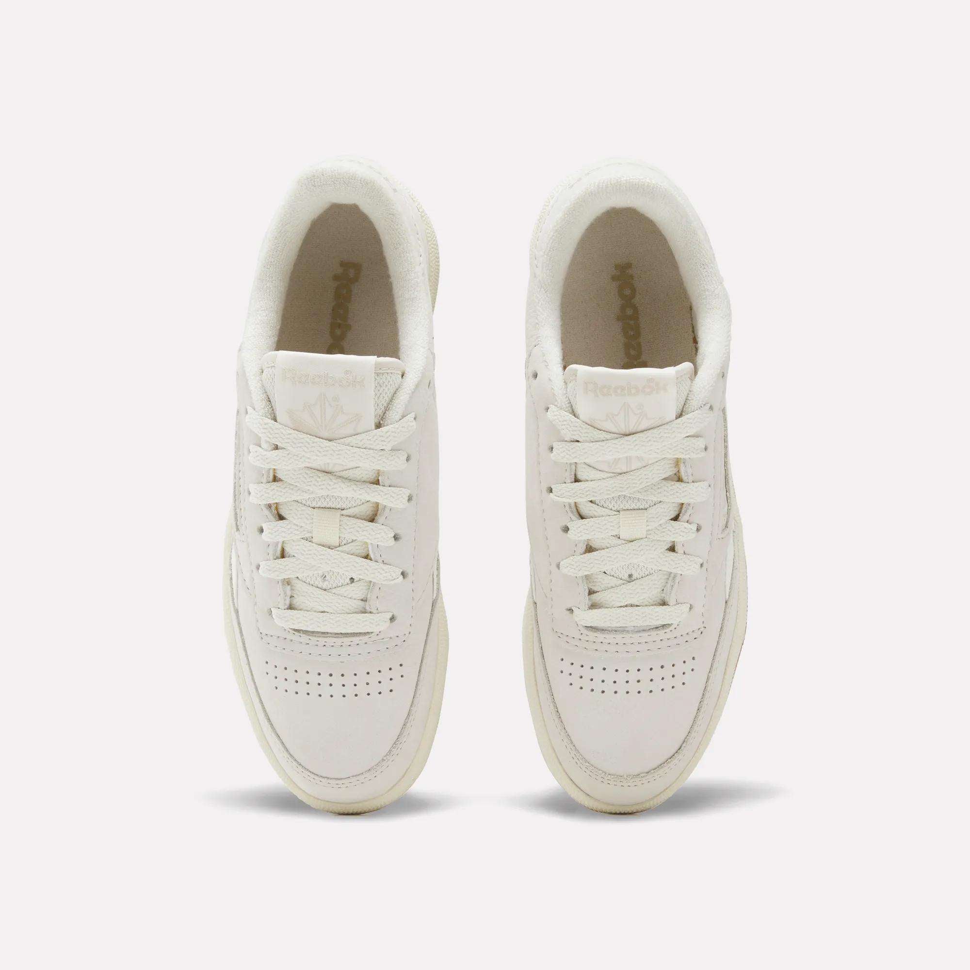 A pair of Women's Club C Revenge Shoes by Reebok in white, seen from above with visible laces, perforated toe areas, and Reebok logos on both the tongue and insole.