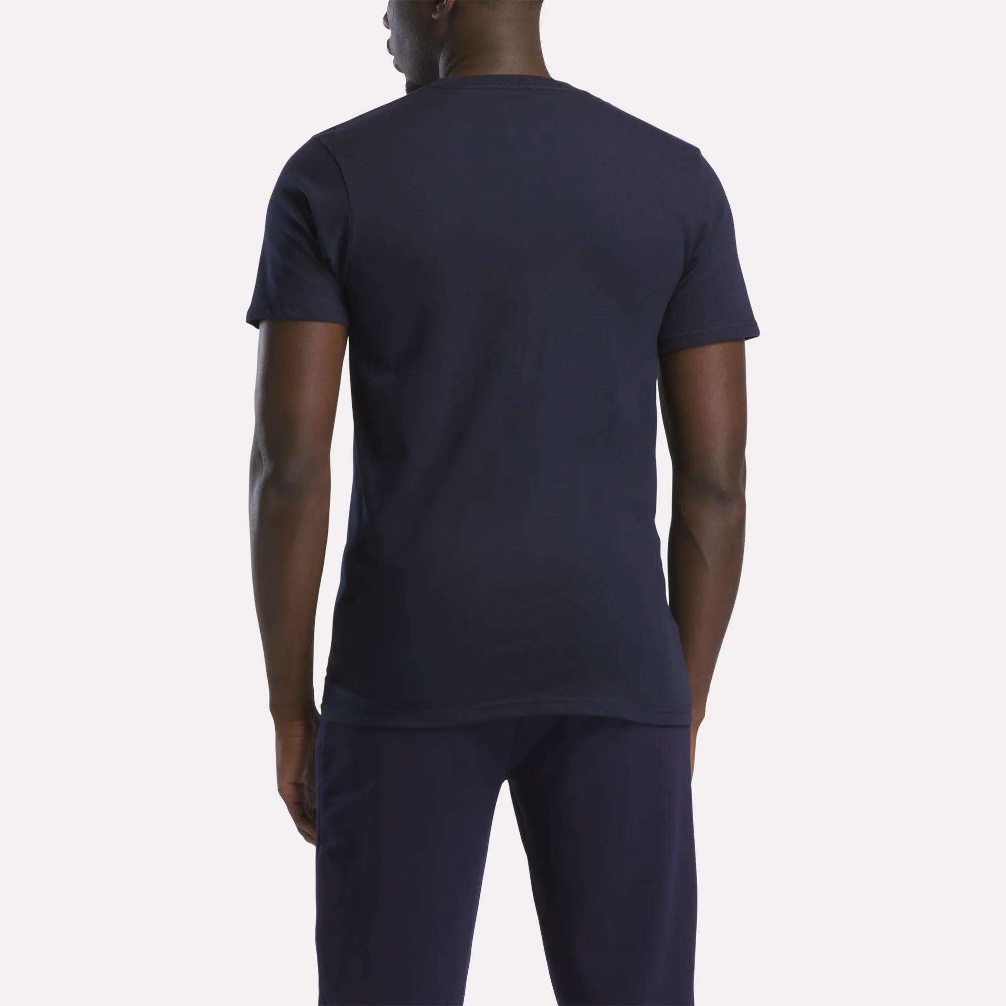 A person stands with their back to the camera, wearing a relaxed fit Reebok Men's Small Logo T-Shirt in dark navy and matching pants, set against a light background.