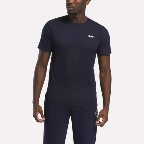 A man stands against a plain light background wearing a fitted Reebok Men's Small Logo T-Shirt and matching navy blue pants.