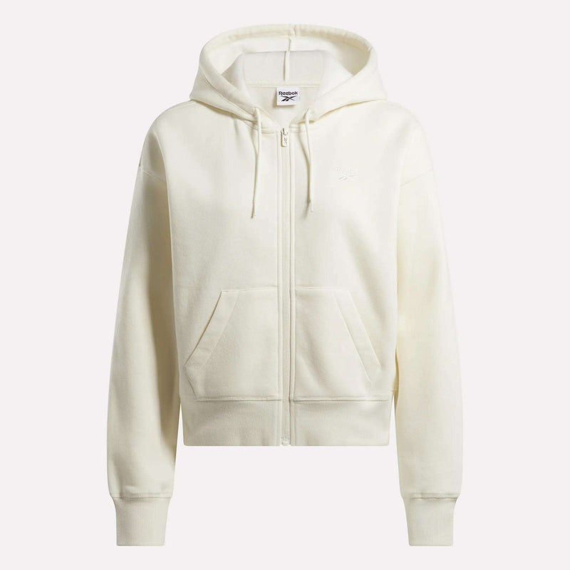 The Women's Cropped Full-Zip Hoodie by Reebok is off-white with a hood, drawstrings, long sleeves, front pockets, and a subtle chest logo. Displayed against a light background.