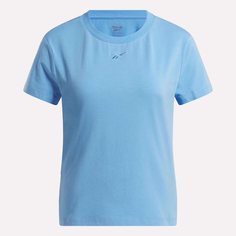 The Reebok Women's Graphic Glow Top is a light blue, short-sleeve shirt featuring a small embroidered logo at the center chest and a plain design with no other patterns.