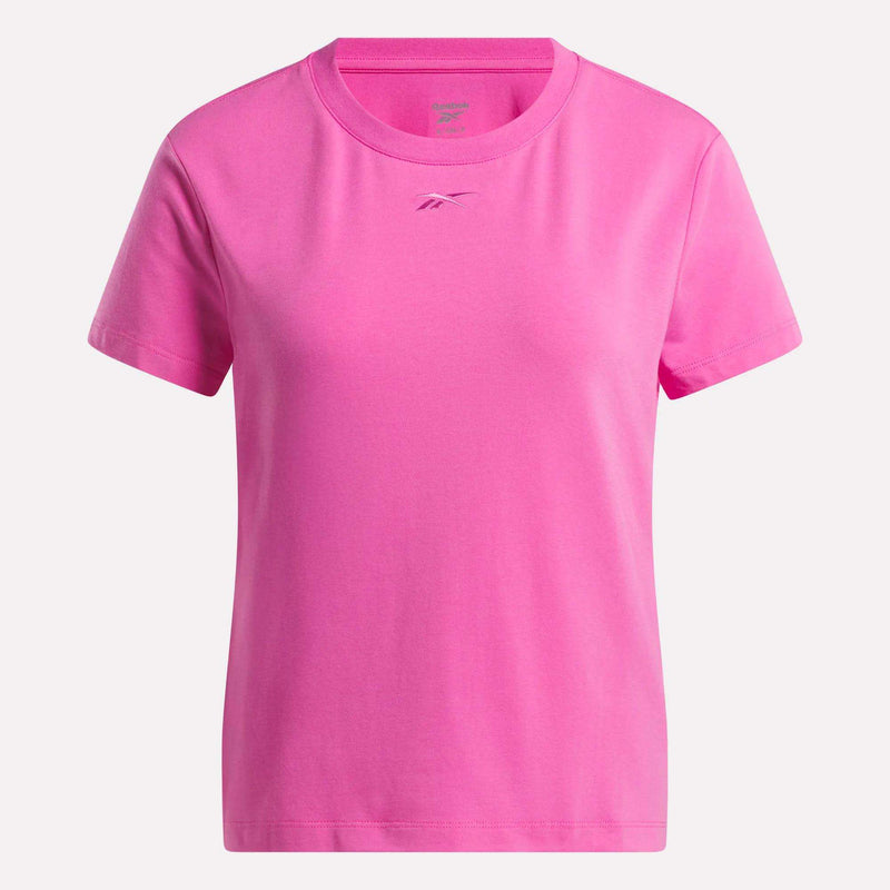 The Women's Graphic Glow Top by Reebok is a pink, short-sleeved shirt with a round neckline and a subtle embroidered logo on the chest, shown against a white background.