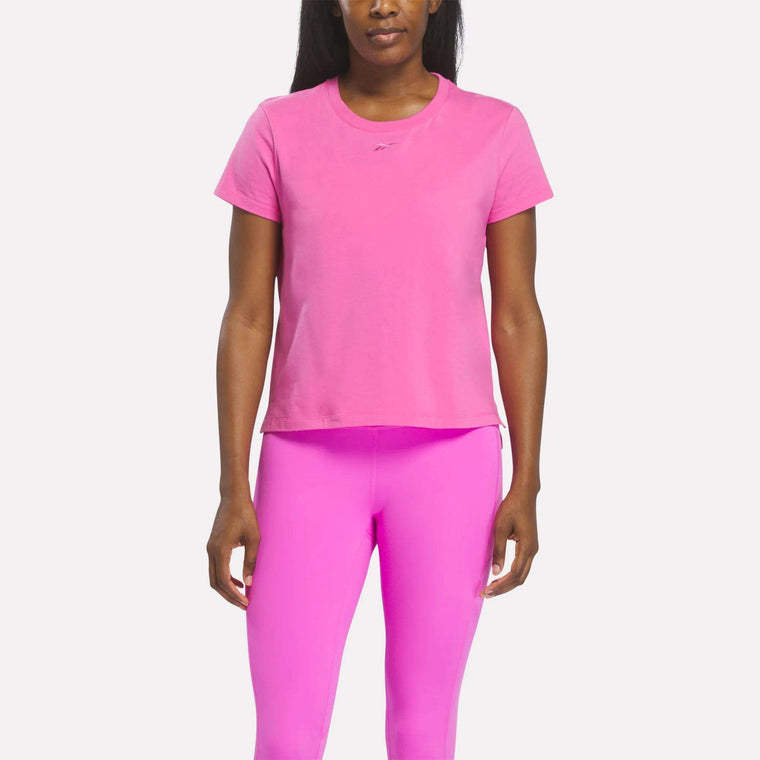 A person stands facing forward wearing a Vector Virtual Pink Women's Graphic Glow Top by Reebok with matching pink leggings against a plain white background.