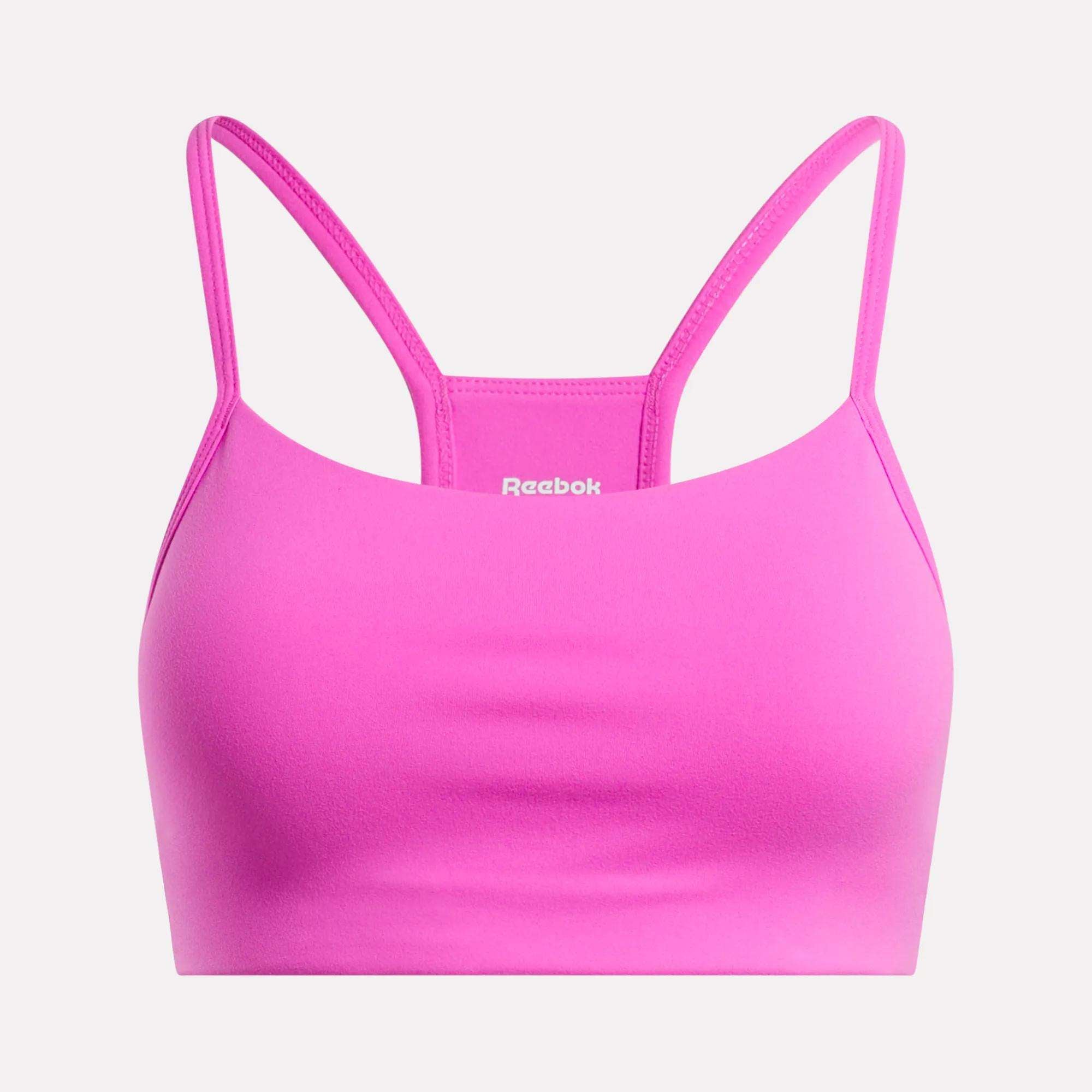 The Reebok Women's Low-Impact Sports Bra is bright pink with thin adjustable straps and a smooth, simple design. The white Reebok logo appears on the front center. Ideal for light-impact training.