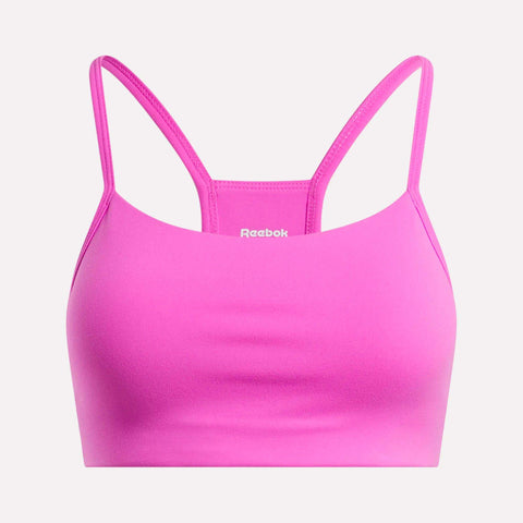 The Reebok Women's Low-Impact Sports Bra is bright pink with thin adjustable straps and a smooth, simple design. The white Reebok logo appears on the front center. Ideal for light-impact training.