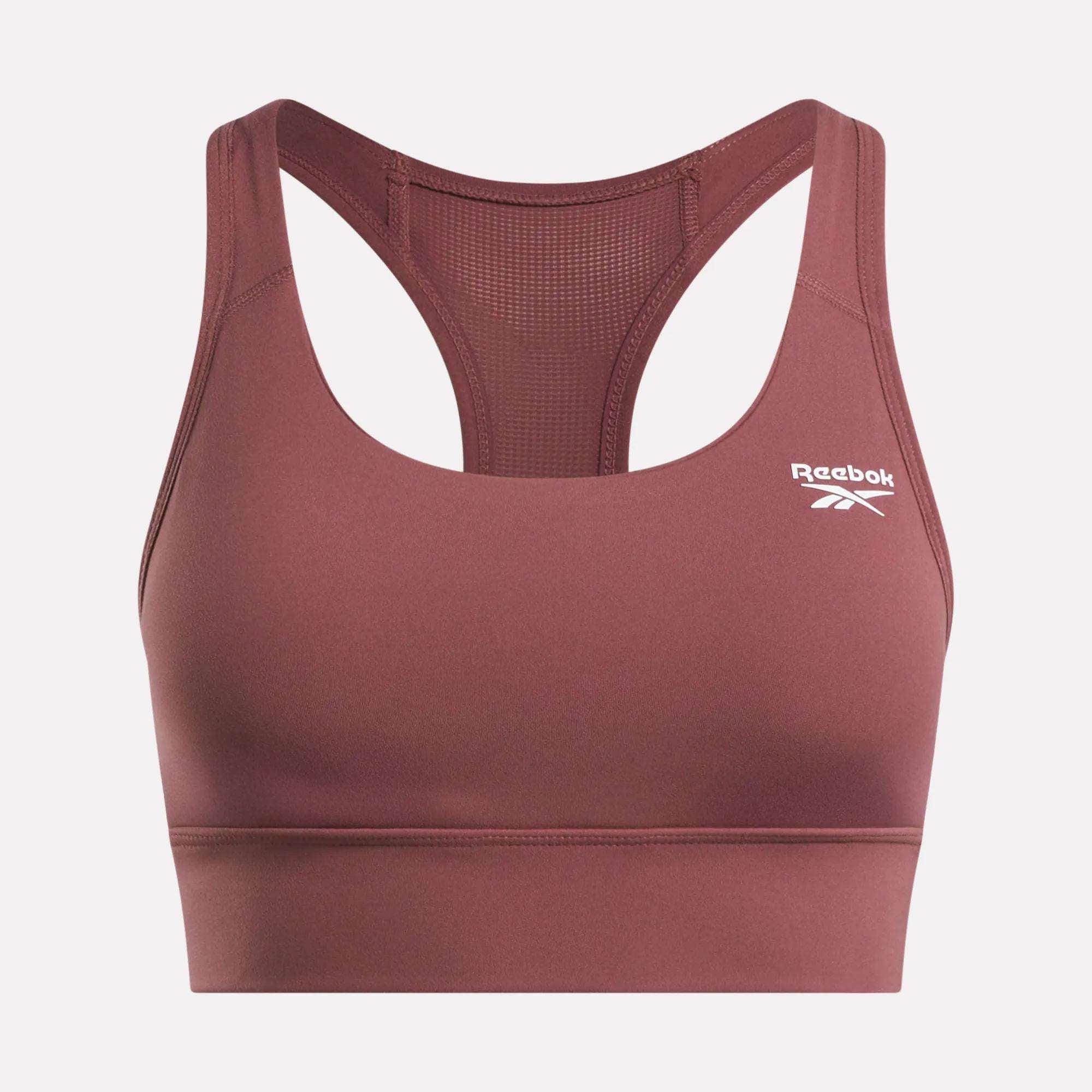 The Reebok Women's Rush Medium-Impact Sports Bra in mauve features a racerback design, mesh back panels for breathability, and a white logo on the front—perfect for medium-impact workouts.