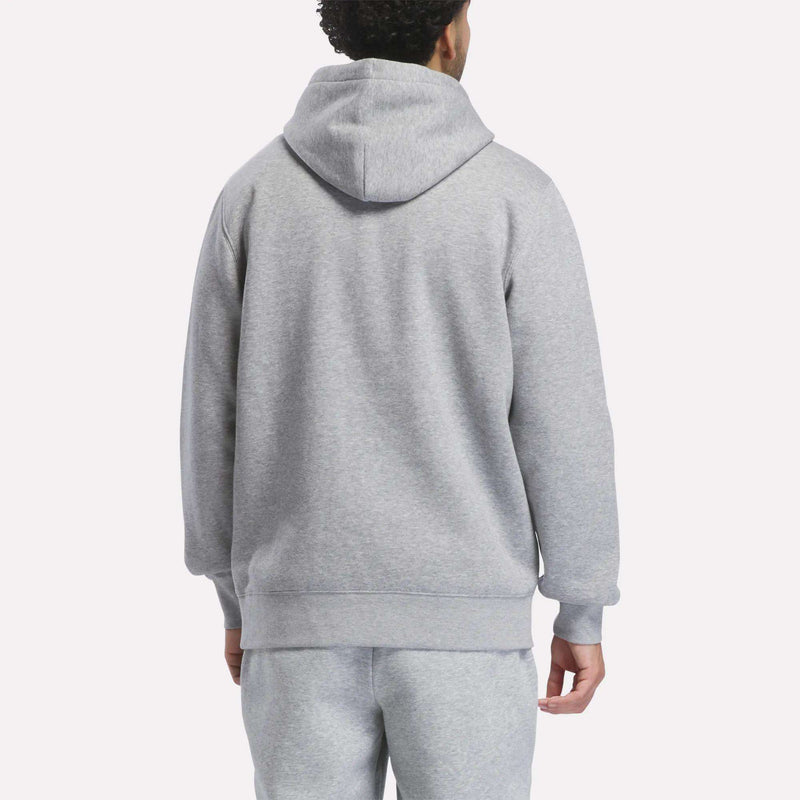 A person is standing with their back to the camera against a plain white background, wearing the men’s Patent Hoodie by Reebok in gray, which features an embroidered logo, paired with matching gray sweatpants.