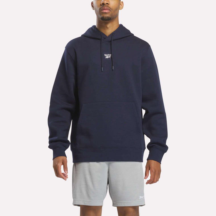 A person wearing the Men's Finisher Hoodie by Reebok in Vector Navy, featuring a small white logo on the chest, and light gray shorts stands facing forward against a plain background.