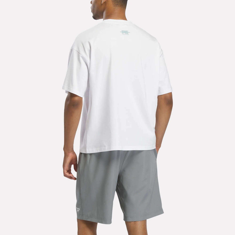 A person stands facing away, wearing a loose Reebok X F45 Training Graphic T-Shirt and light gray shorts against a plain light background.