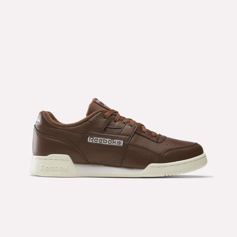 A Formal Brown/Ftwr White/Chalk Reebok Workout Plus Shoe featuring a white sole, iconic side logo patch, brown laces, and a low-top silhouette is presented in profile against a plain white background—these classic sneakers embody the timeless style of the Workout Plus line.