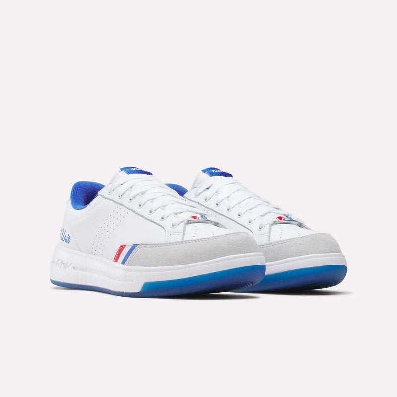 The Reebok x G-Unit G6 Men’s Shoes by Reebok feature a white low-top silhouette with blue accents, gray suede overlays, perforated side panels, and bold red and blue stripes near the sole, channeling the streetwise aesthetic of early 2000s hip-hop and iconic G-Unit design. Presented against a plain white background.
