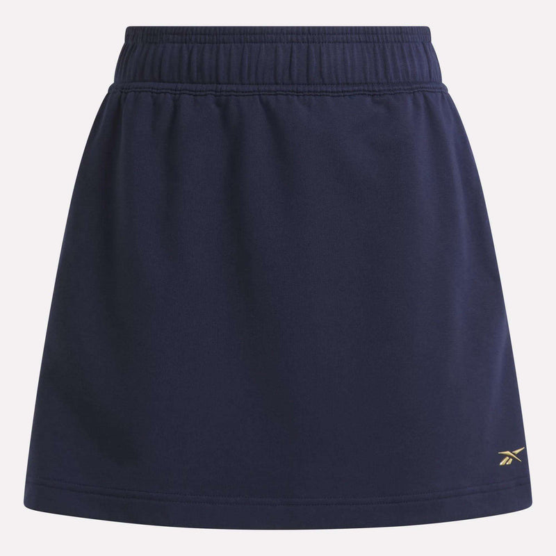 The Women's Logo Skirt by Reebok is a navy blue sports skirt with an elastic waistband, a small yellow logo near the right hem, and is made from a comfortable cotton blend.