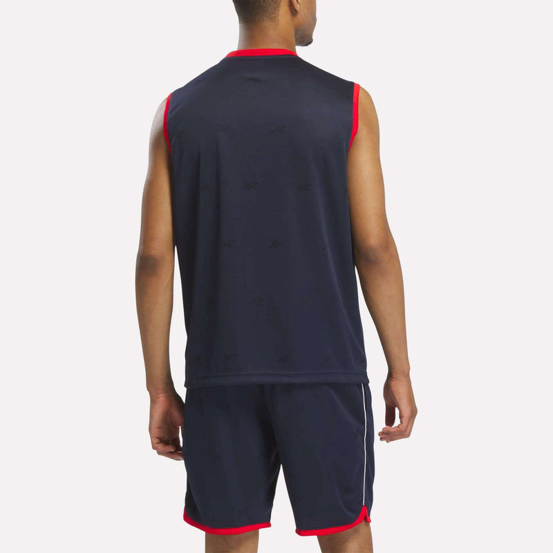 A man faces away, wearing a Reebok Men's United Jersey Tank and matching shorts in navy with red trim and white stripes, resembling a soccer jersey, against a plain light background.