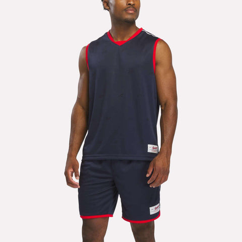 A man wears the Reebok Men's United Jersey Tank and matching shorts with red trim. He stands against a plain white background, looking slightly to the side.
