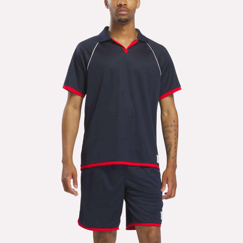 A man stands facing forward against a plain background, wearing a Reebok Men's United Jersey Polo Shirt in Vector Navy.