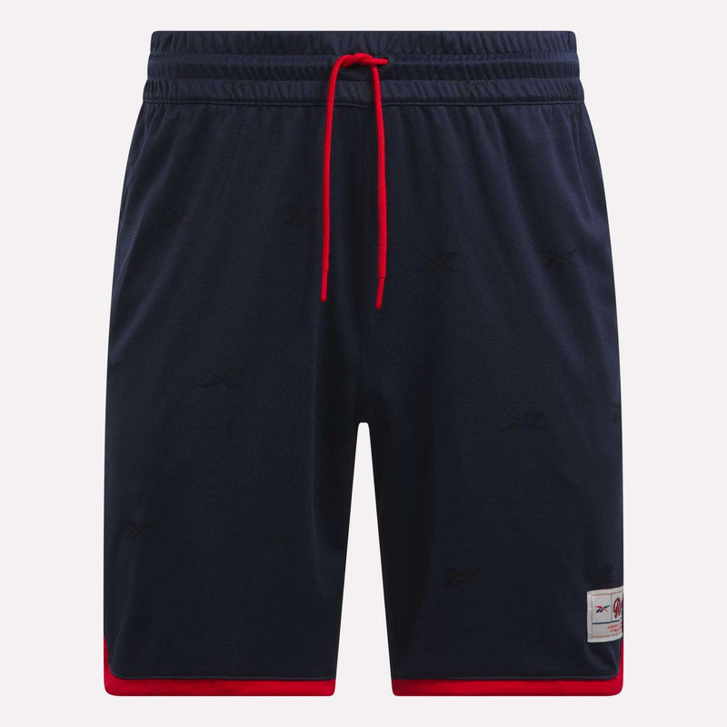 The Reebok Men's United Shorts 9" are navy blue lightweight polyester shorts with red trim at the leg openings, a red drawstring, subtle logo patterns, and a small logo patch near the left hem.