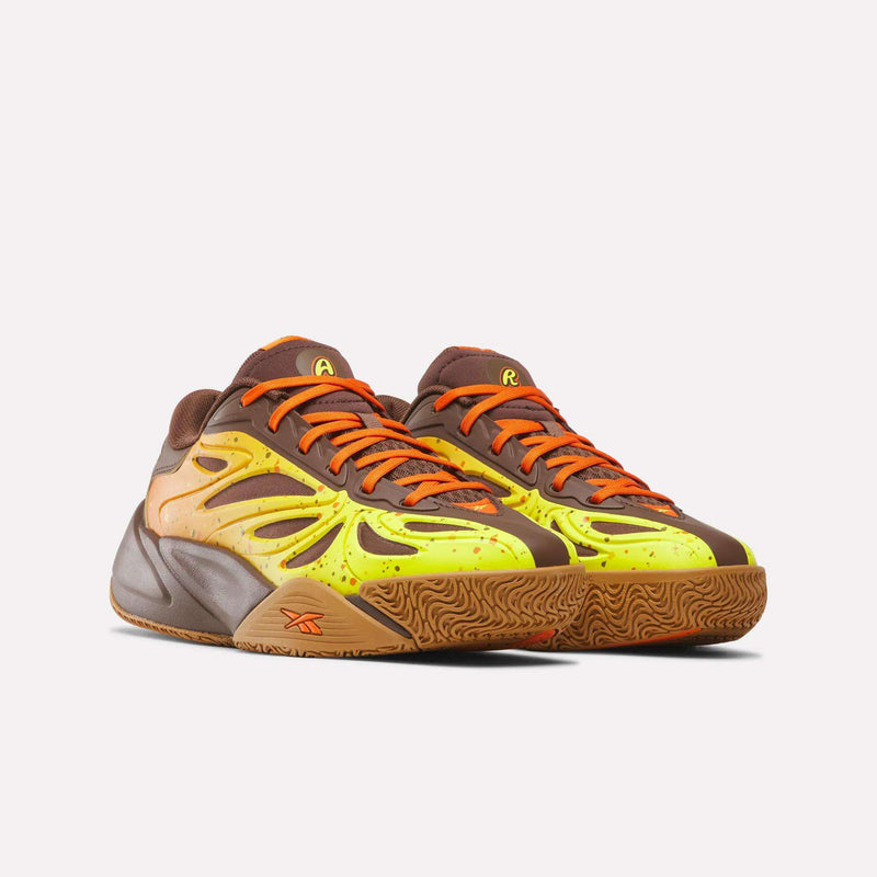 The Reebok Reese’s x Angel Reese 1 Basketball Shoes for big kids feature brown, yellow, and orange accents with vibrant patterns and orange laces, displayed against a light background.