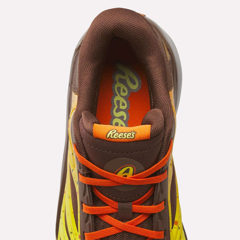 A top-down view of the Reese’s x Angel Reese 1 Basketball Shoe by Reebok, featuring a brown and yellow color scheme with orange laces and the Reebok x Reese’s logo on the tongue and insole.