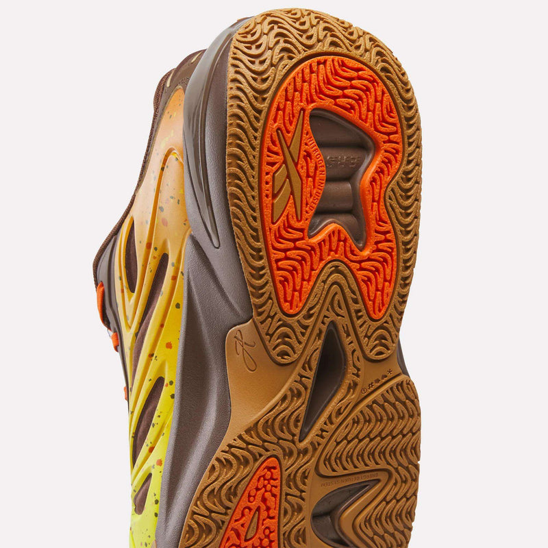 A close-up of the sole of the Reese’s x Angel Reese 1 Basketball Shoes highlights its intricate orange and brown tread patterns as seen from below. The upper features yellow and brown gradients with wavy designs, showcasing Reebok’s innovative Energy Return System inspired by the brand’s collaboration with Angel Reese.