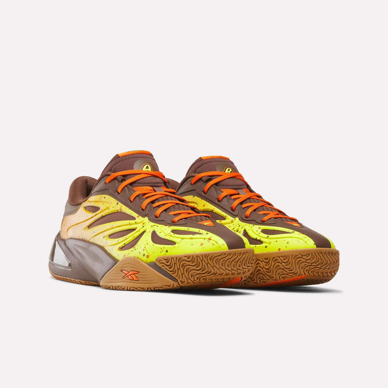 The Reese’s x Angel Reese 1 Basketball Shoes by Reebok showcase a striking brown, orange, and yellow color scheme with bright orange laces and wavy side patterns, set against a plain white background. Featuring an advanced Energy Return System for superior performance, these sneakers combine standout style with dynamic comfort.