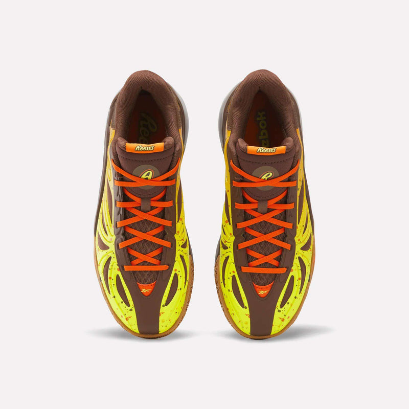 Top view of a pair of Reebok Reese’s x Angel Reese 1 Basketball Shoes, featuring brown uppers, neon yellow accents, and bright orange laces on a white background. These sneakers are designed with Reebok’s innovative Energy Return System for enhanced comfort and performance.