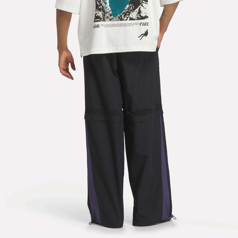 Reebok x A Herd of Bison Transform Pants featuring loose-fitting black ripstop fabric with purple side panels and drawstring hems.