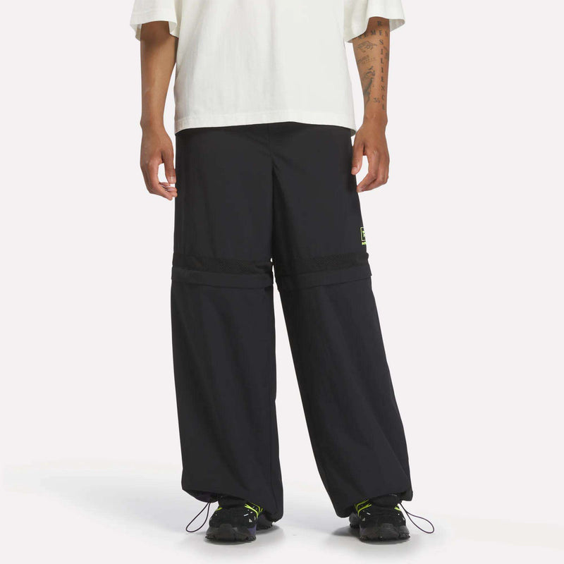 Person wearing black Reebok x A Herd of Bison Transform Pants with a horizontal mesh panel at the thighs, lime green logo detail, and black athletic shoes.