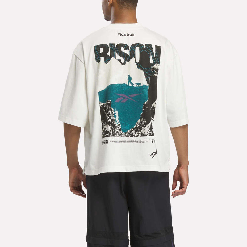 A person wearing an oversized off-white Reebok x A Herd of Bison Graphic Tee featuring a mountain scene with a hiker and dog, the word BISON, and small printed text.