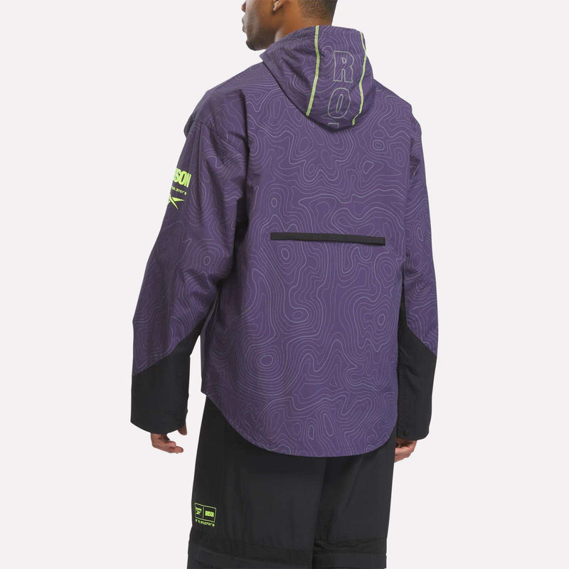 A person wears a Reebok x A Herd of Bison Packable Jacket: a purple hooded windbreaker with a white topographic map pattern, neon green text, and black accents on the sleeves and hem.
