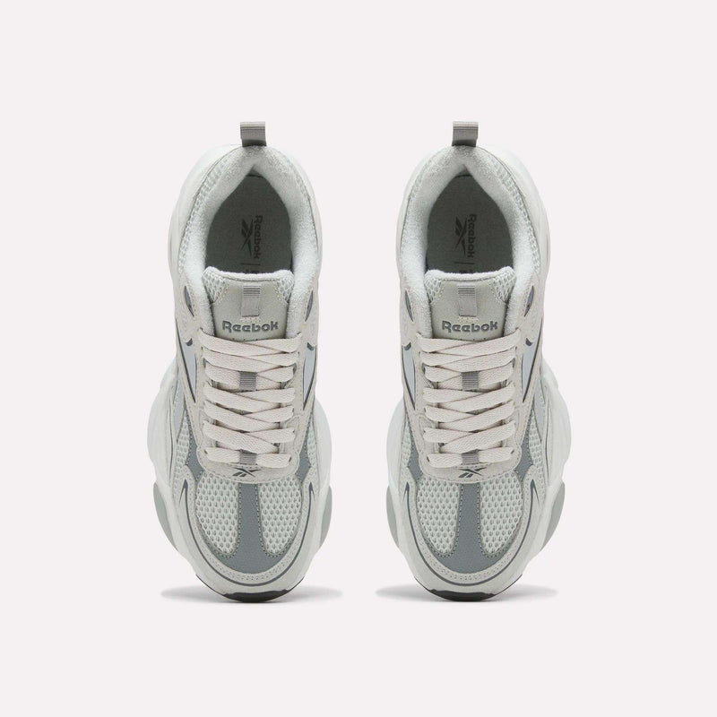 A pair of Reebok Men’s Charge Shoes in white and gray is displayed from above, highlighting the laces, mesh design, and chunky sole. The cushioned midsole provides comfort during workouts, while the Reebok logo appears on the tongue of each shoe.