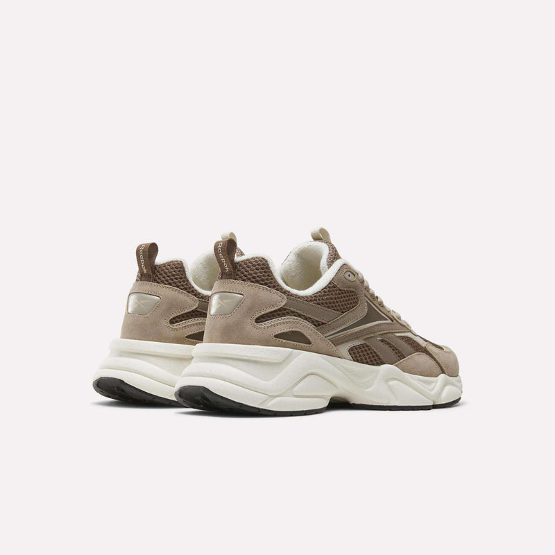 A pair of Reebok Men’s Charge Shoes in brown and beige, featuring chunky white soles, mesh and suede accents, and heel pull tabs. These heritage-inspired men’s athletic shoes are positioned slightly angled away from each other on a plain white background.