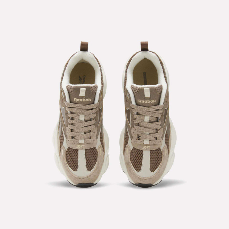 Top view of a pair of beige and brown Reebok Men’s Charge Shoes with white soles and mesh detailing, placed side by side on a plain light background—perfect athletic footwear for men featuring a heritage-inspired design.