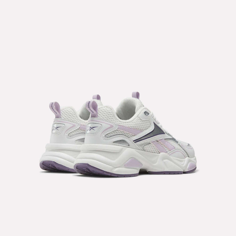 A pair of Reebok Women’s Charge Shoes in white and lavender are displayed from the back and side on a plain light background. Featuring mesh and suede construction with lavender accents and thick soles, these sneakers are perfect for your next workout.