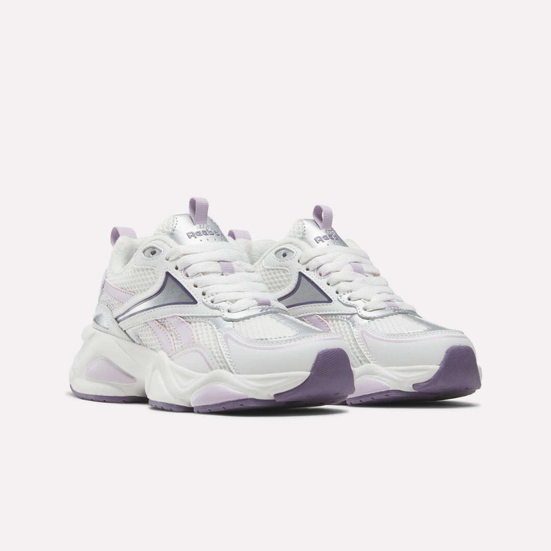A pair of Reebok Women’s Charge Shoes featuring light purple and silver accents, thick soles, mesh and leather details, a cushioned midsole, and purple outsoles, displayed side by side on a white background.