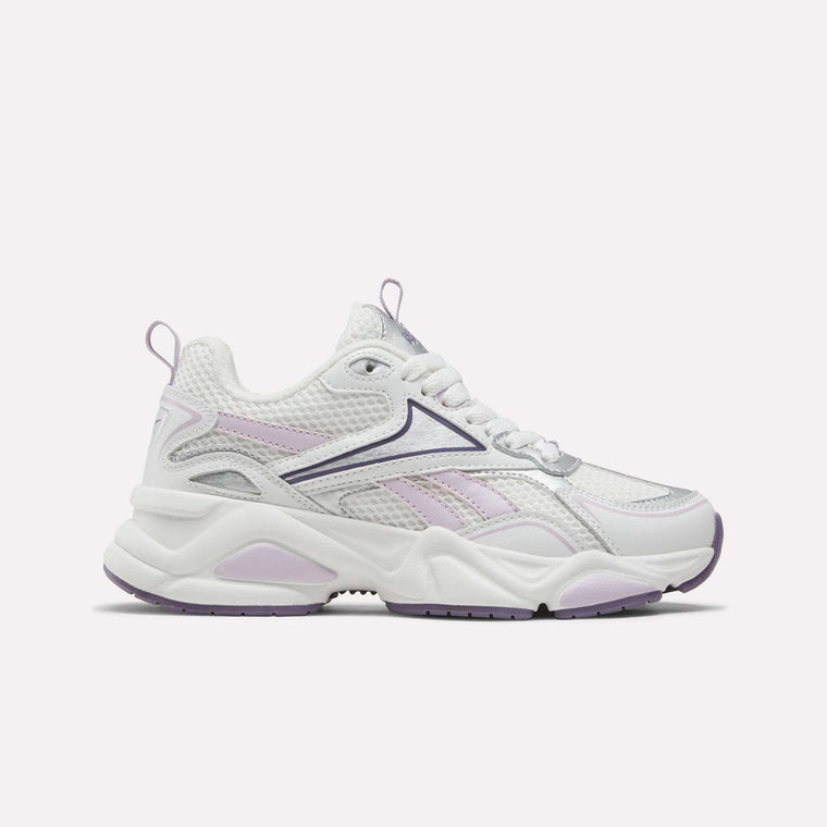 Reebok Women’s Charge Shoes in White/Purple feature a chunky sole, cushioned midsole, breathable mesh upper, and lace-up closure. Shown against a plain light background, these versatile athletic sneakers are perfect for training.