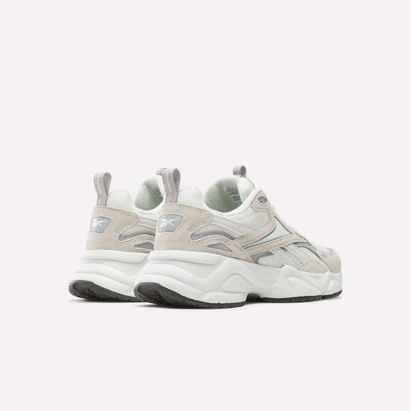 A pair of Reebok Women’s Charge Shoes in light beige and white, featuring gray accents, the Reebok logo on the heel, chunky white soles, and black tread, positioned on a plain white background and angled slightly to the left.