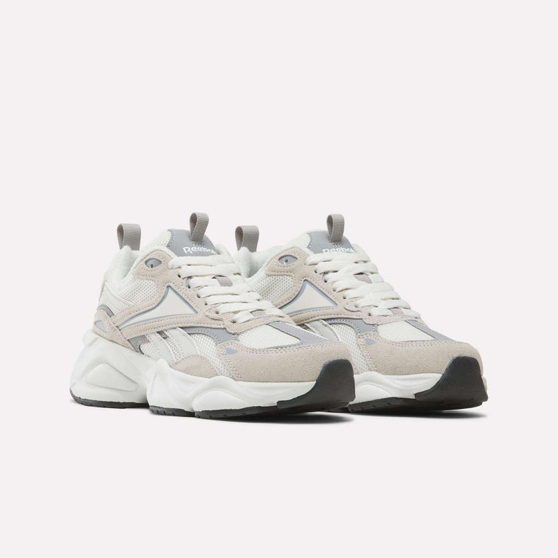 A pair of Women’s Charge Shoes by Reebok, featuring beige, white, and gray tones with chunky soles, mesh panels, and suede accents, is displayed against a plain white background. These athletic shoes for women seamlessly combine style and comfort for everyday wear.
