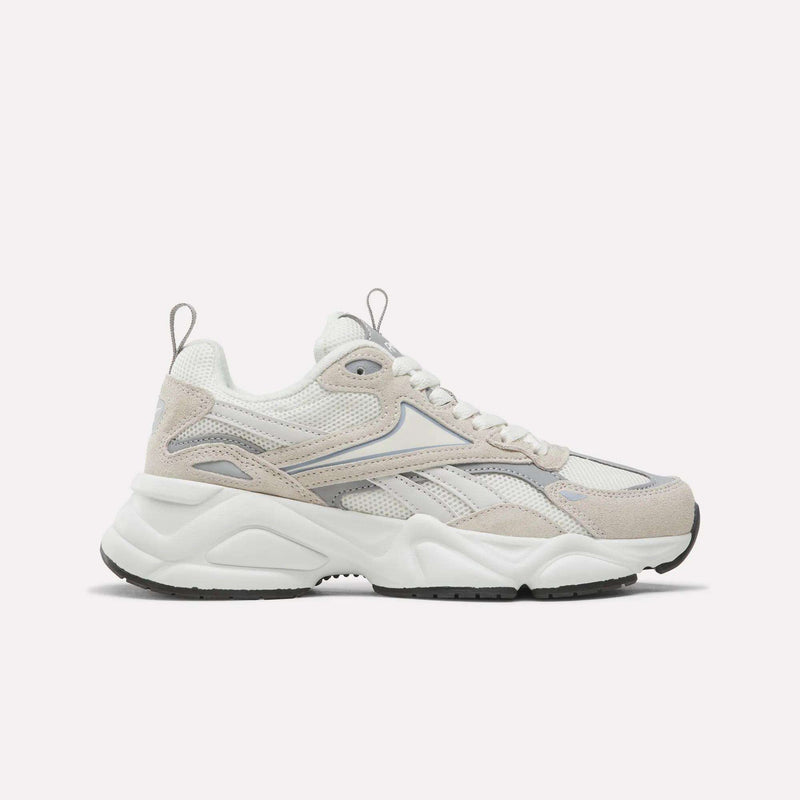 The Reebok Women’s Charge Shoes in White/Beige feature a chunky sole, mesh and suede panels, and a lace-up design. Shown in side profile against a plain light background, they are an ideal choice for anyone seeking stylish women’s athletic footwear.