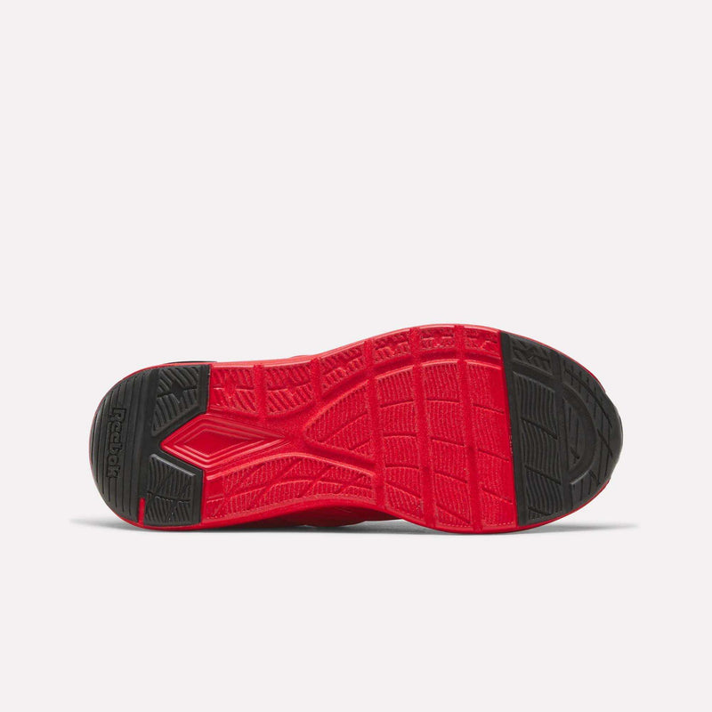 The image displays the bottom view of a red and black Reebok Zome Flare Shoes - Big Kids sole, featuring textured grip patterns and geometric tread designs that emphasize the brand’s commitment to comfortable footwear for children.
