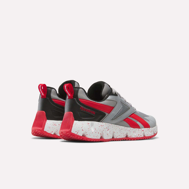 The Reebok Pyro Storm Shoes - Big Kids are lightweight running shoes with gray, red, and black accents. They feature a speckled white midsole and bold red outsoles and are shown from the back and side angles against a plain background.